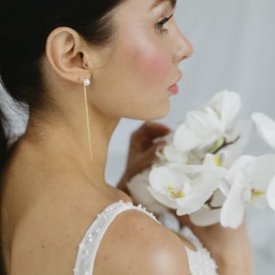 Dunkelhaarige Braut mit Blumen in der Hand und Brautohrringen
