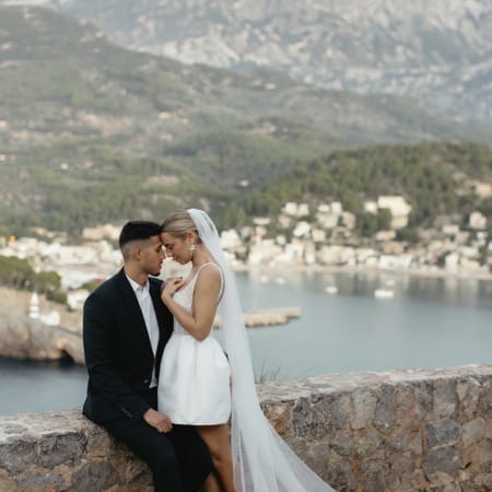 Brautpaar an Mauer. Die Braut trägt ein kurzes Brautkleid und einen langen Schleier