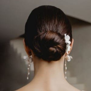 Braut mit dunklen Haaren trägt strengen Dutt als Brautfrisur mit Headpiece